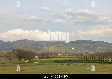 Ländliche Panoramalandschaft in der Nähe von Spello (Spello), Umbrien, Italien, mit sanften Hügeln, bewirtschafteten Feldern, verstreute Häuser und ein bewölkter Himmel. Stockfoto