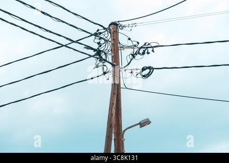 Nahaufnahme eines hölzernen Versorgungsmasts mit verwickelten elektrischen Kabeln gegen einen hellen Himmel. Selektiver Fokus. Stockfoto