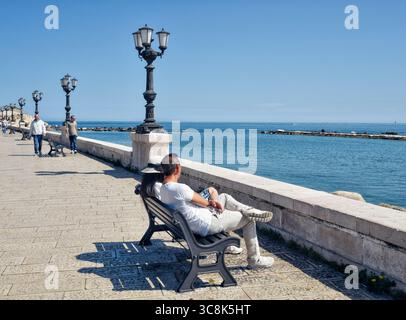 Ein Paar sitzt auf einer Bank und blickt aufs Meer, Bari, Apulien, Italien Stockfoto