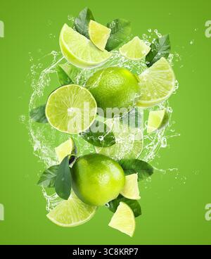 Frische Limetten und Spritzwasser in der Luft vor grünem Hintergrund Stockfoto