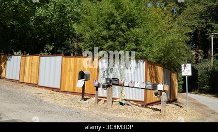 Eine Reihe von ländlichen Briefkästen steht am Eingang zu einer privaten Fahrt in Nordkalifornien, mit einem Holz- und Metallzaun im Hintergrund Stockfoto