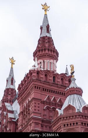 Das hoch aufragende Gebäude aus rotem Backstein zeigt ein kompliziertes Design mit mehreren Türmen und dekorativen goldenen Elementen vor einem grauen Himmel in Moskau Stockfoto
