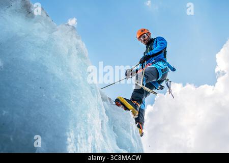 Bergsteiger in leuchtenden Farben, die während des Lenin Gipfels unter klarem Himmel mit schneebedeckten Gipfeln im Hintergrund Serac auf dem eisigen Gletscher absichern. Extrem A Stockfoto