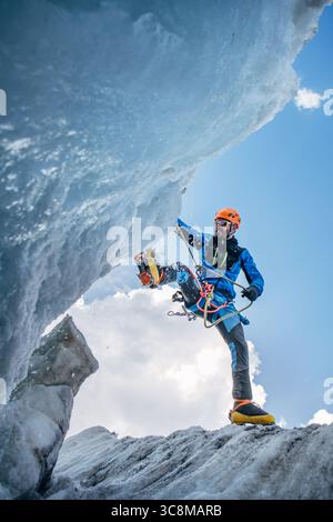 Bergsteiger in pulsierender Ausrüstung hüpft über Gletscherspalten beim Aufstieg des Lenin Gipfels unter klarem Himmel mit schneebedeckten Gipfeln im Hintergrund. Extremer Akt Stockfoto