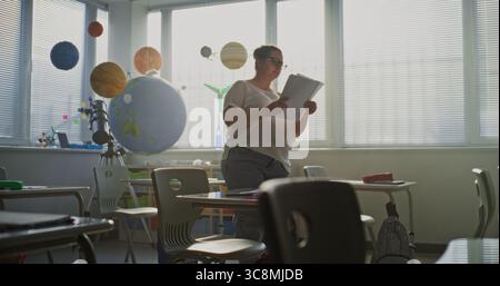 Lehrerin legt Arbeitsblätter mit Schreibübungen für die Schüler vor dem Unterricht an. Lehrer organisieren Raum für Schulprüfung im Klassenzimmer, Arbeit in der modernen Grundschule. Dolly Shot. Stockfoto