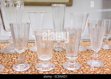 Set leerer Vintage-Wodka-Gläser. Vintage-Trinkbecher aus Glas werden ordentlich auf einem gemusterten Stoffhintergrund präsentiert. Brillen variieren in Größe und Form, Showc Stockfoto