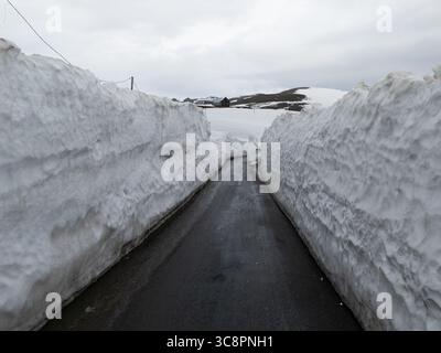 Aus der Vogelperspektive auf einer schmalen Straße, die durch hoch aufragende Schneefelder führt und einen starken Kontrast zwischen dem dunklen Asphalt und der strahlend weißen Landschaft offenbart, Goderdzi, Adjara, Georgia. Stockfoto