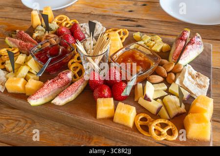 Gemischte Käseplatte mit frischen Feigen, Erdbeeren, Nüssen, Brezeln und Obstmarmelade auf rustikalem Holztisch. Käseplatte. Vorspeise und Partyessen Stockfoto