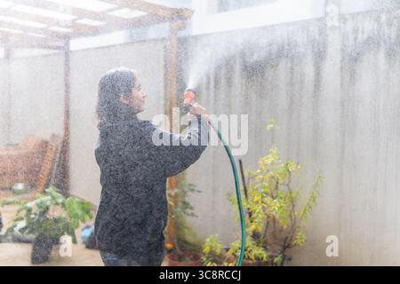 Eine junge Frau, die ihren Garten an einem sonnigen Tag mit einem Schlauch tränkt Stockfoto