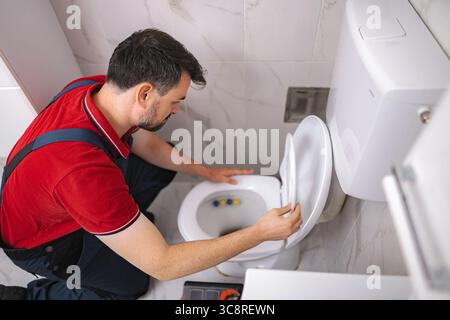 Klempner inspiziert die Toilettenschüssel im Badezimmer während des Hausbesuchs Stockfoto