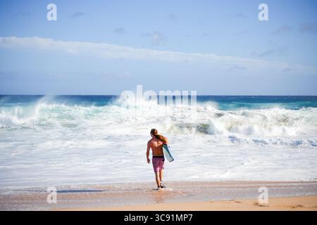 Bodyboarder sehen sich unter hellem Himmel mit der aufragenden blauen Welle konfrontiert, die den Nervenkitzel und die Energie extremer Meeressportarten in kristallklarer Brandung einfängt Stockfoto