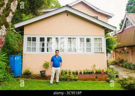 Mann steht vor einem traditionellen Landhaus mit weißen Fenstern und Garten in üppiger grüner Umgebung. Stockfoto