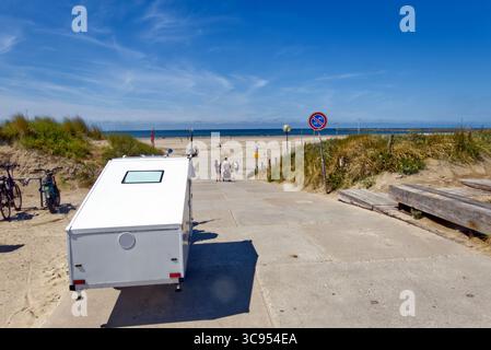 Freizeitfahrzeug parkt an der Sandküste, Sonnenlicht beleuchtet Strandbesucher, die in den Sommerferien in der Nähe der Küste spazieren Stockfoto