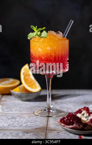 Sonnenaufgangscocktail in einem hohen Glas mit Strohhalm, Granatapfel, Orange, zerstoßenem Eis Stockfoto