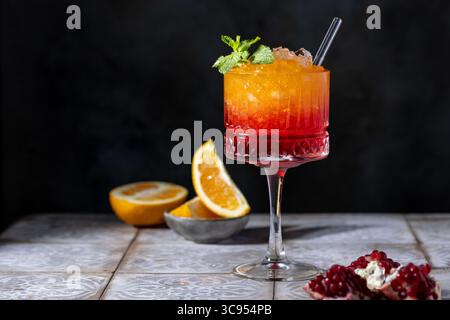 Sonnenaufgangscocktail in einem hohen Glas mit Strohhalm, Granatapfel, Orange, zerstoßenem Eis Stockfoto