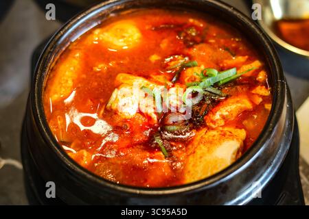 Sundubu-jjigae, der beliebte koreanische Tofu-Eintopf, serviert in einem traditionellen schwarzen Töpfertopf. Stockfoto