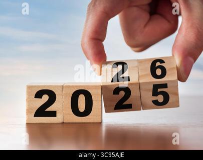 Neujahrskonzept von 2025 bis 2026. Eine Hand ändert einen Holztischkalender. Jubiläum- und Änderungskonzept. Stockfoto