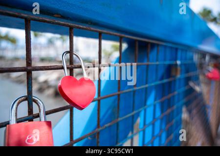 Ein blauer Zaun mit roten Herzen drauf. Die Herzen sind an einem Metalltor befestigt. Das Tor ist mit einem Vorhängeschloss verschlossen Stockfoto