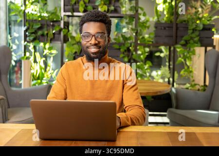 Afroamerikanischer Geschäftsmann im legeren Outfit, der geschäftliche Aufgaben auf dem Laptop verwaltet Stockfoto