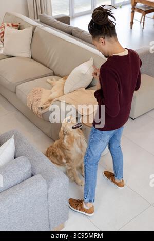 Mann, der auf Golden Retriever zeigt und Ingwerkatze auf Sofa mit gemusterten Kissen im Wohnzimmer Stockfoto
