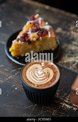 Ein Stück Kuchen, serviert mit einer Tasse Cappuccino mit Latte Art, auf einem rustikalen Holztisch. Gemütliche und einladende Café-Szene. Stockfoto