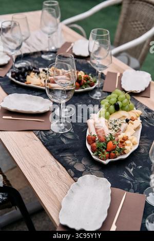 Ein wunderschön gestalteter Tisch mit Charcuterie, frischem Obst und eleganten Gläsern, ideal für Essen und Zusammenkünfte im Freien Stockfoto