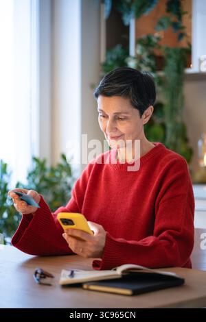 Entspanntes Lächeln Online-Einkäufe mit Debitkarte mit Smartphone. Online-Shopping, E-Commerce Stockfoto