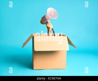 Menschliche Hand, die Megaphon aus offener Pappschachtel vor leuchtendem blauem Hintergrund hält Stockfoto