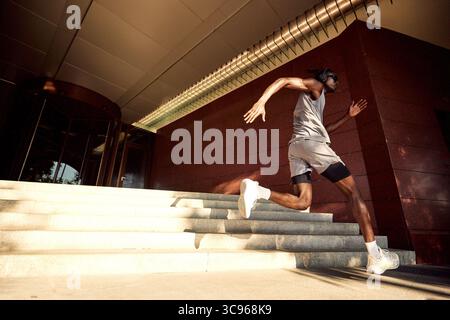 Eine motivierte Person demonstriert körperliche Fitness und Engagement, indem sie eine Treppe in der Nähe eines modernen Gebäudes hinaufspringt. Das Bild erfasst Bewegungen und Stockfoto