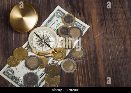 Kompass mit Euro-Münzen, Dollarschein auf Holzoberfläche. Stockfoto