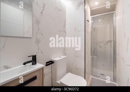 Modernes Bad mit Marmorwänden, Glasdusche und elegantem Waschbecken. Das Design ist minimalistisch und modern, in neutralen Farben und klar Stockfoto