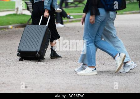 Stuttgart, Deutschland. August 2025. Drei Leute laufen mit Gepäck durch einen Park, einer von ihnen zieht einen schwarzen Trolley-Koffer hinter sich. Quelle: Markus Lenhardt/dpa/Alamy Live News Stockfoto