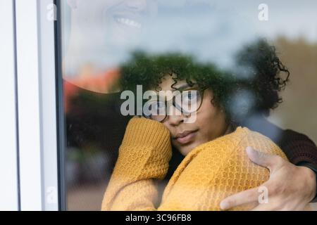 Verschiedene Paare, die sich zu Hause an einer Glasscheibe lehnen, mit Strickpullover und Brille Stockfoto