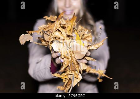 Nahaufnahme einer nicht erkennbaren Frau mit einer Handvoll trockener gelber Blätter, die im Herbst vom Baum gefallen sind und sie vor der Kamera zeigen, bevor sie sie werfen Stockfoto