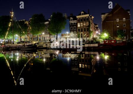 Der mondbeleuchtete Waalseilandsgracht-Kanal in Amsterdam Binnenstad leuchtet mit beleuchteten Hausbooten und jahrhundertealten Fassaden, die sich nachts im ruhigen Wasser spiegeln. Stockfoto