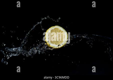 In Scheiben geschnittene Zitrone mit Wasserspritzer auf schwarzem Hintergrund. Stockfoto