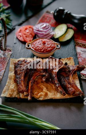Köstlich gegrillte Lammkoteletts, serviert mit frischem Gemüse und würziger Sauce auf einer Platte aus schwarzem Schiefer für ein Gourmet-Erlebnis Stockfoto