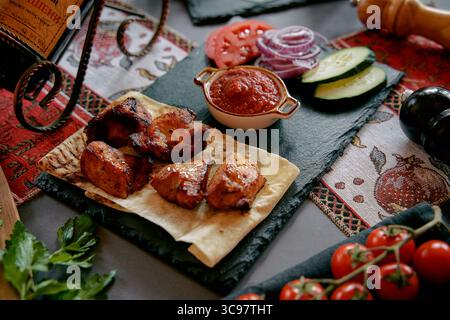 Eine köstliche Platte mit gegrillten Hähnchenspießen, serviert mit frischem Gemüse und würziger Sauce auf einem rustikalen Tisch Stockfoto