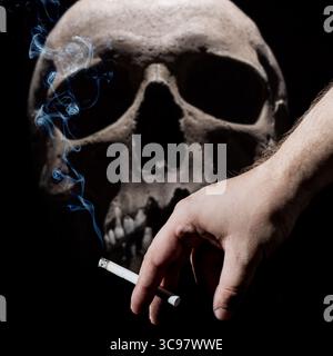 Männliche Hand, die eine rauchende Zigarette auf schwarzem Hintergrund mit einem Schädel hält. Gesundheitsgefährdungskonzept Stockfoto