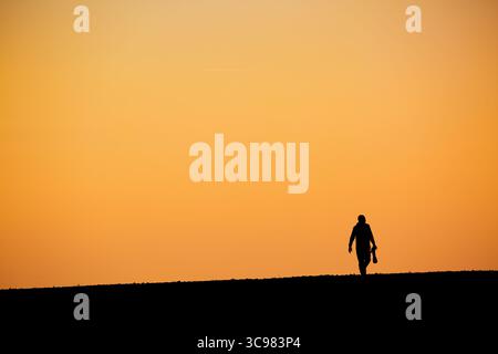 Silhouette Mann mit großem Teleobjektiv vor orangem Hintergrund des Sonnenuntergangs Stockfoto