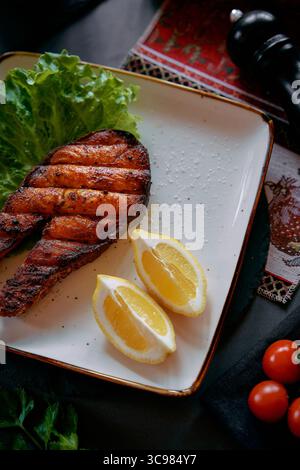 Köstlich gegrilltes Lachsfilet auf einem Teller mit frischem Salat, Zitronenscheiben und bunten Kirschtomaten für eine helle und gesunde Mahlzeit Stockfoto