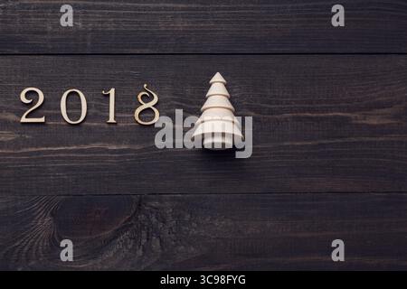 Happy New Year 2018 von echten Holzfiguren mit einer Tanne auf dunklem hölzernem Hintergrund. Stockfoto