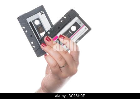 Weibliche Hand mit roten Nägeln, die zwei Retro-Audiokassettenbänder auf weißem Hintergrund halten Stockfoto
