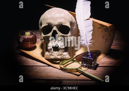 Literaturkonzept. Altes Tintenständer, Lupe, Schädel, Kerze und Feder auf alter Vintage-Rolle und hölzernem Hintergrund Stockfoto