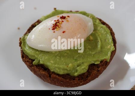 Avocadotoast mit pochiertem Ei auf einem weißen Teller, Nahaufnahme Stockfoto
