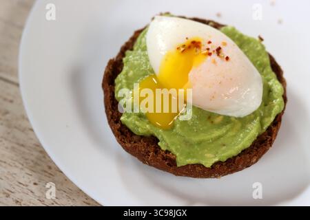 Avocadotoast mit pochiertem Ei auf einem weißen Teller, Nahaufnahme Stockfoto