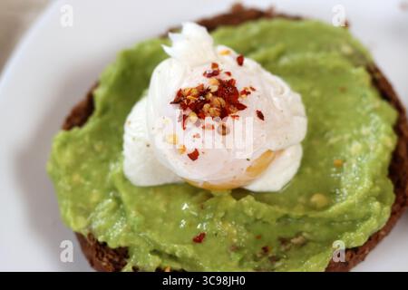Avocadotoast mit pochiertem Ei auf einem weißen Teller, Nahaufnahme Stockfoto
