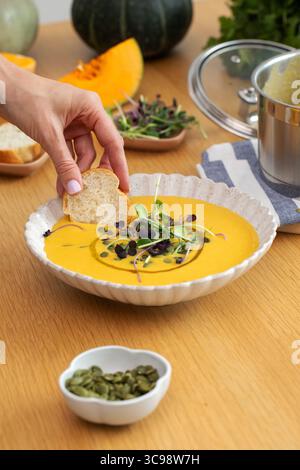 Brot von Hand in Gemüsesuppe mit Mikrogrün und Kürbis auf dem Tisch tauchen Stockfoto