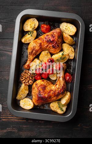 Hähnchenschenkelviertel gebacken mit Kartoffeln, Tomaten, Knoblauch und Kräutern in Backblech, Draufsicht. Herzhafte hausgemachte Mahlzeit - Hühnchen und Gemüse. Stockfoto