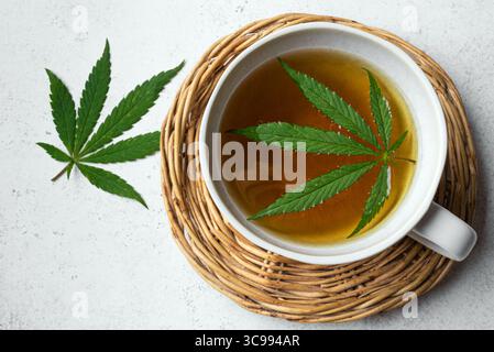 Tasse Hanf Kräutertee und grüne Hanfblätter, Blick von oben. Natürliches beruhigendes Getränk für gesundes Schlafen. Stockfoto